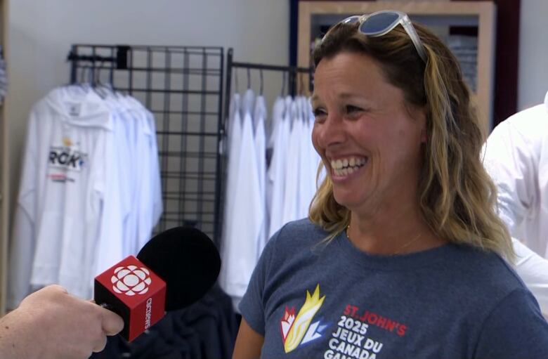 A woman with sunglasses on her forehead wears a T-shirt that says St. John's 2025 Jeux de Canada Games. 