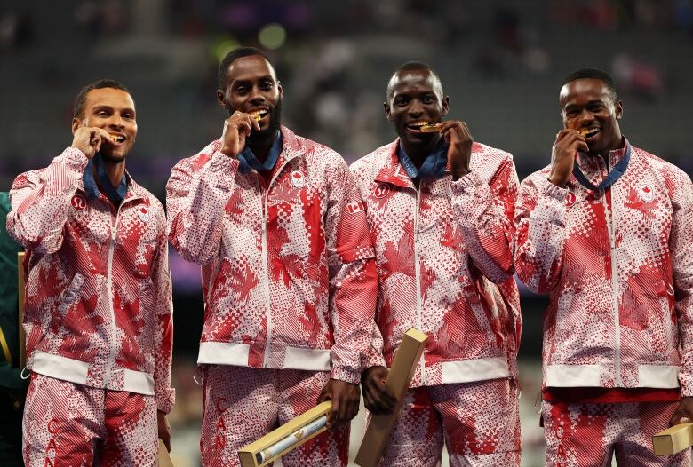 Four male sprinters are seen biting their gold medals.