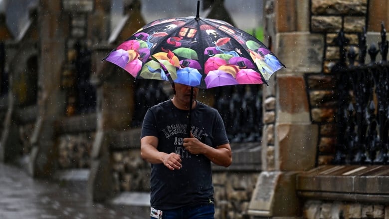 A man with a colourful umbrella walks on a city street during a rainstorm.