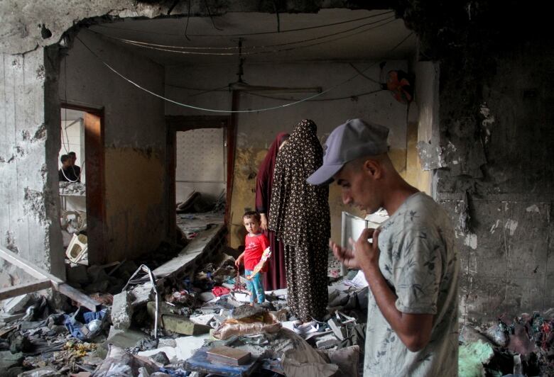 People stand amid debris inside a building damaged by a rocket attack.