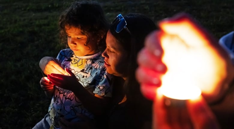 A woman stands by a candle. 