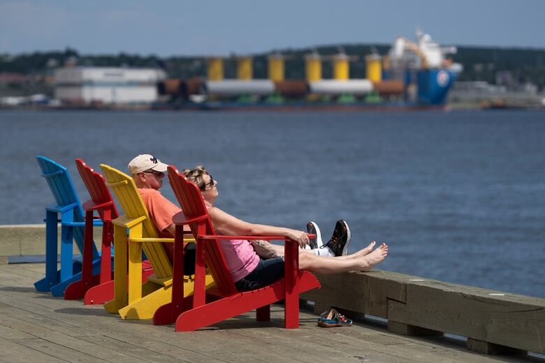 Two people are lying on deck chairs with their feet up. The Halifax Harbour and a large ship are in the background.