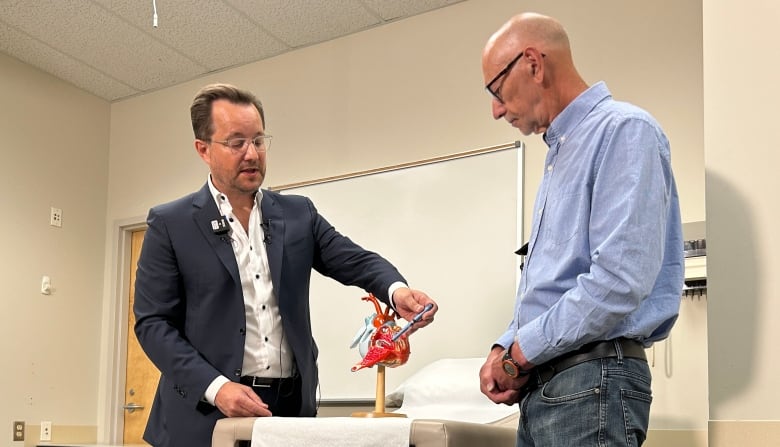 A doctor showing a patient how a pacemaker is placed in his heart, using a model of a heart