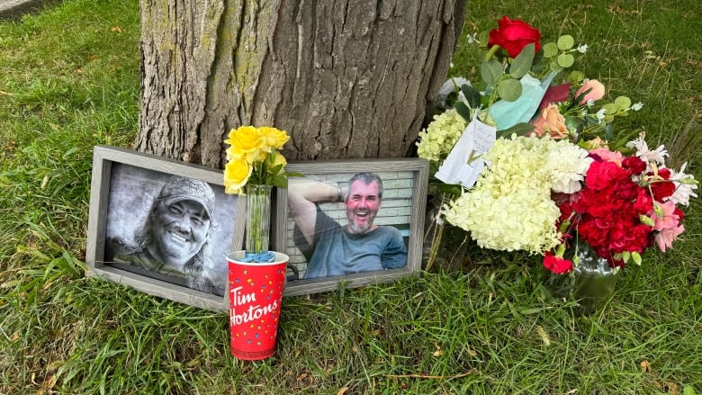 A memorial for 67-year-old Walter Lasher of Greater Napanee, photos, flowers and tim hortons cups surround a tree. 