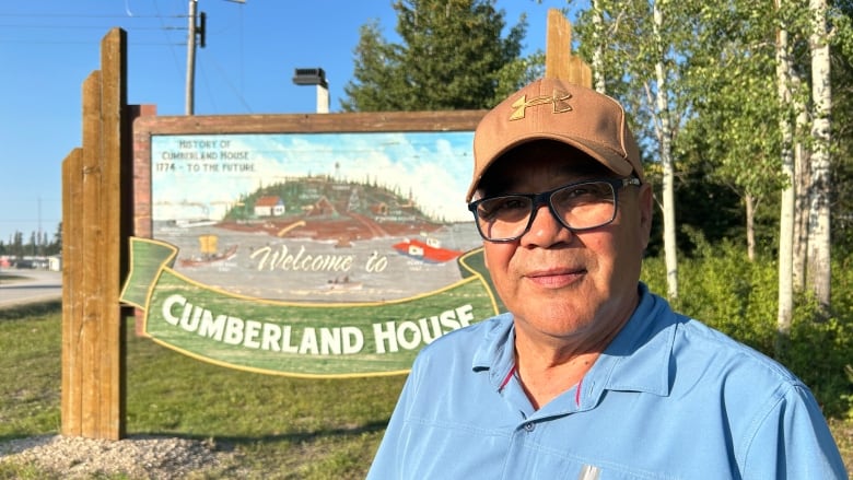 A man in a ball cap and a blue shirt poses in front of a sign that says 