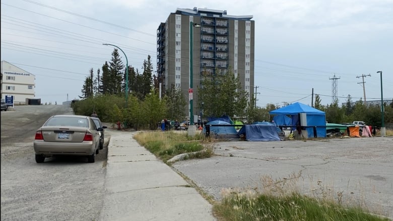 A couple of tents set up in a parking lot with a tall building in the background.