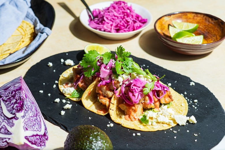 Closeup on 3 fish tacos topped with red cabbage and cilantro. 