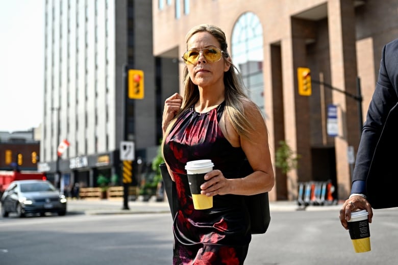 A woman in a black and red top and yellow sunglasses holds a cup of coffee.