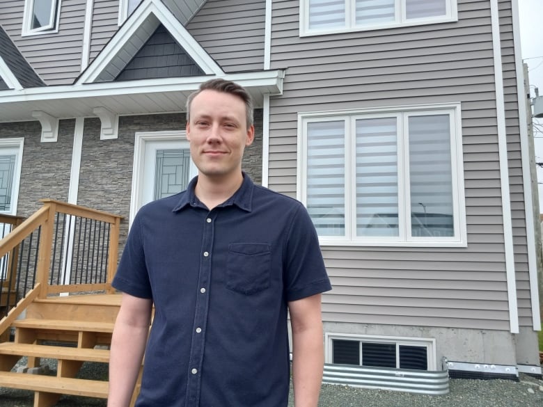 Man in blue dress shirt standing in front of home