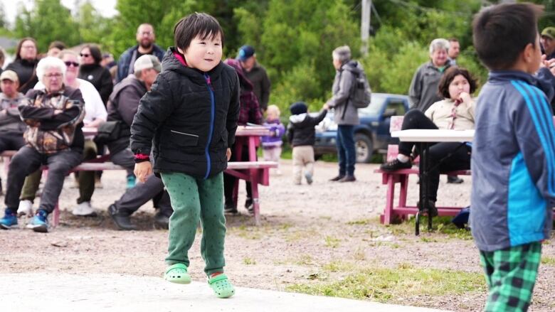 A young boy jumps up and down on a stage with other people behind him. 