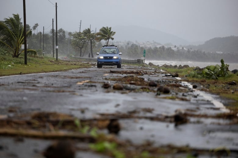 A car drives through a seaside road littered with debris