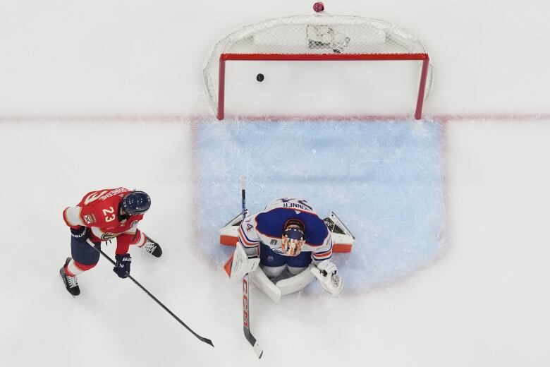 A hockey player scores on a goalie right by the crease, as seen from above. 