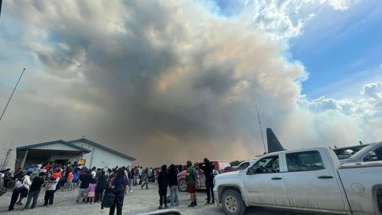 People stand at an airport with smoke billowing in the air