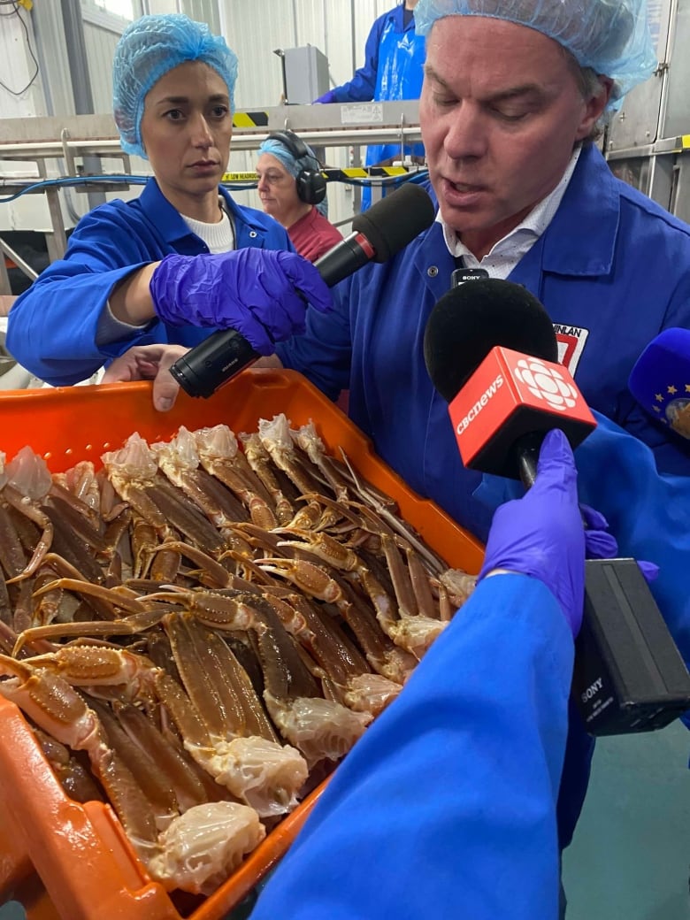 Woman holds mic in mans face as he holds container of crab legs.