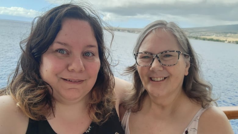 Two people looking at the camera, close-up of them, with water in the background.