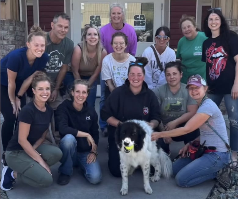 A bunch of people pose for a photo with a black and white dog.