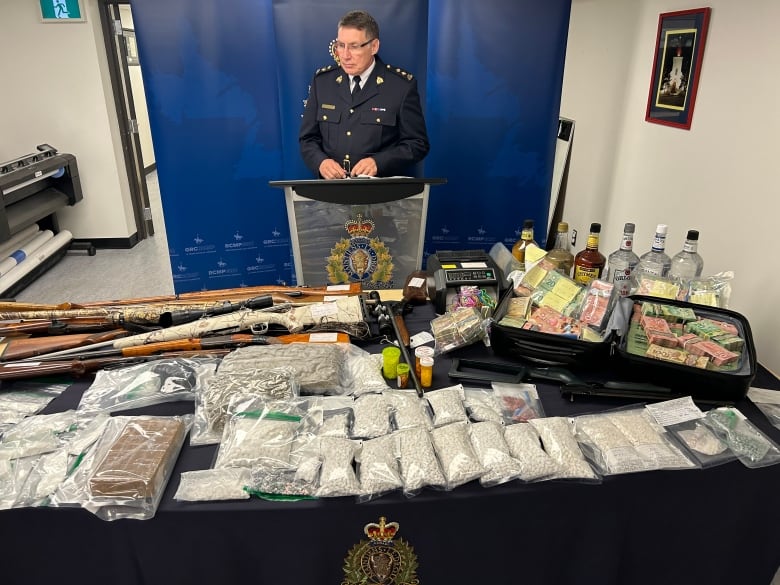 A police officer stands over a large table of pills, guns, cash and liquor.