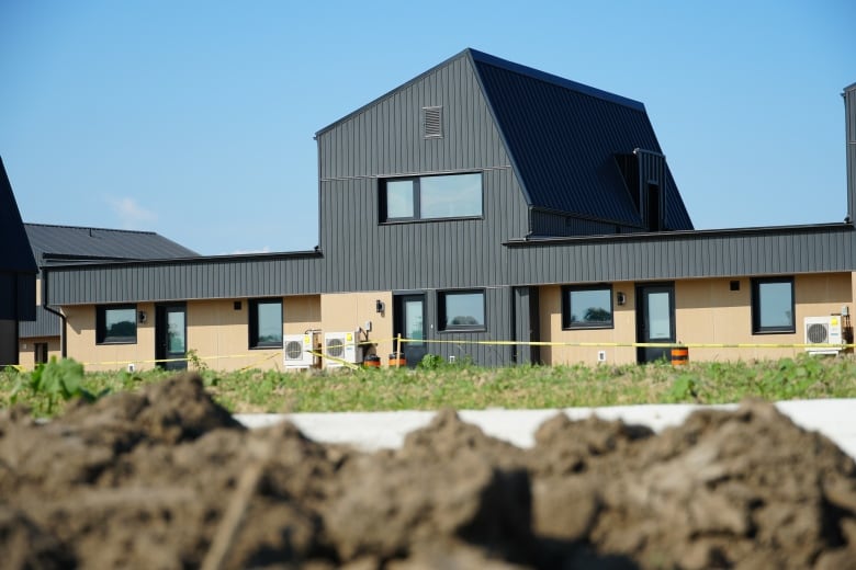 A home with black and brown panels sits in the distance with caution tape close by.