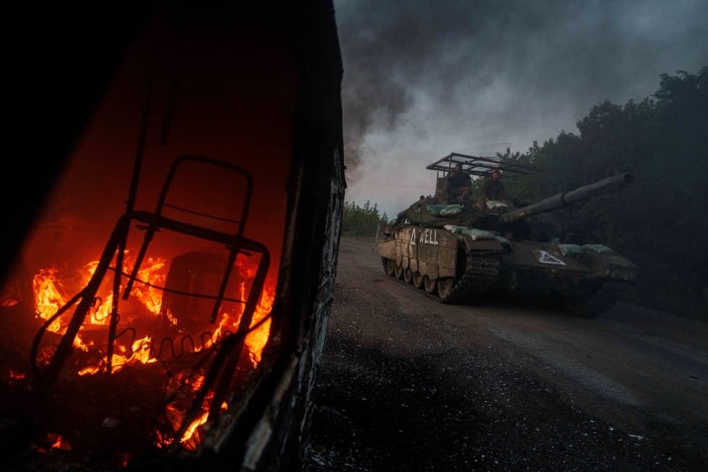 A Ukrainian tank passes by a burning car near the Russian-Ukrainian border, Sumy region, Ukraine, Wednesday, Aug. 14, 2024.