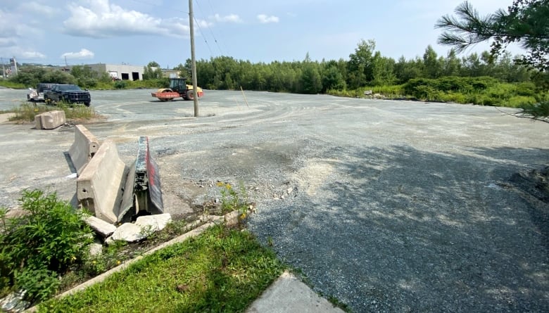 A large gravel piece of land is seen surrounded by trees, with a black truck parked on it and a piece of construction equipment