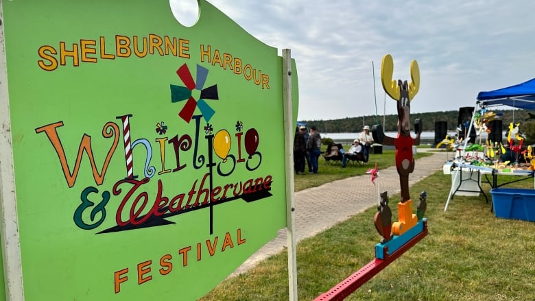 A green sign that reads 'Shelburne Harbour Whirligig and Weather vane festival.'