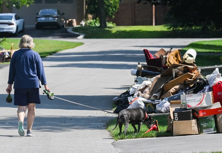 A woman walking her dog next to discarded household items. 