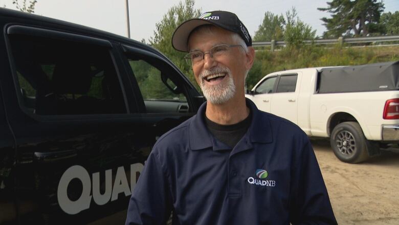 A smiling man in a ballcap and shirt saying 