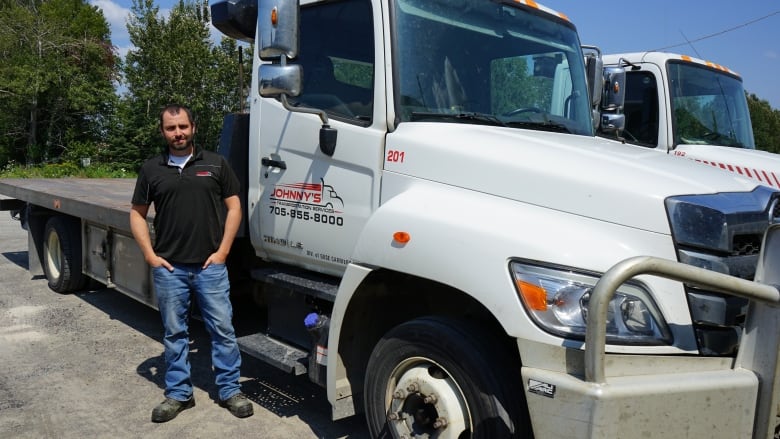 A man poses in front of a tow truck.