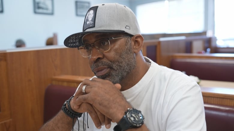 A man wearing glasses, a grey hat and a white T-shirt.