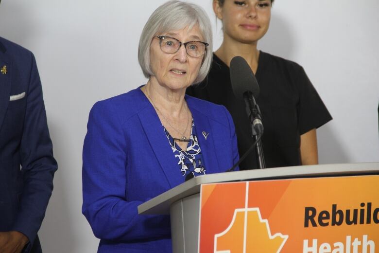 A woman in a blue blazer speaks behind a podium.