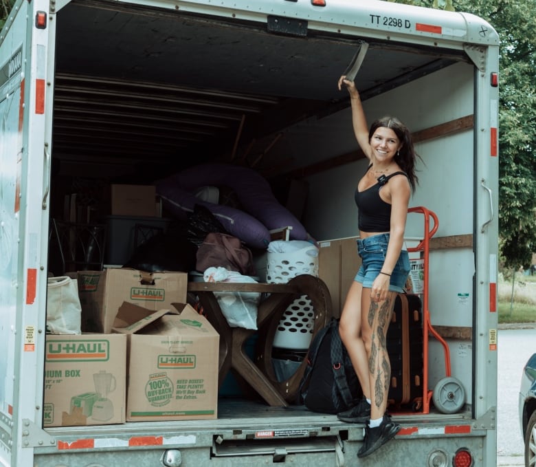 A woman stands on the back of a truck, ready to pull the truck closed. There are boxes inside the truck. 