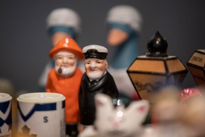 A few salt and pepper shakers lie on a table. In focus are two shakers shaped like sailors, with two others shaped like ducks in the background.