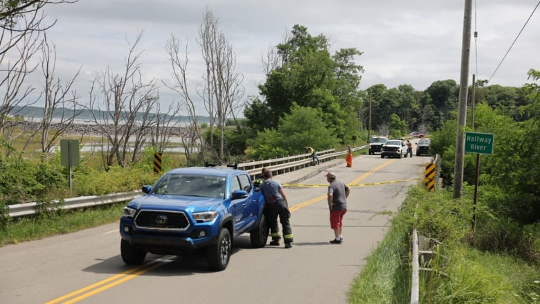 A bridge with yellow caution tape and a number of people and vehicles is shown.