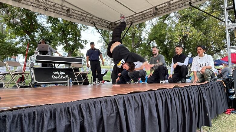 One man posing in a dance move while others cheer and observe