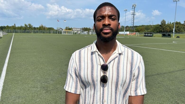 A young man with a mustache and beard stands on a soccer field. 