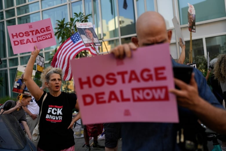 People hold pink signs with red lettering that reads 