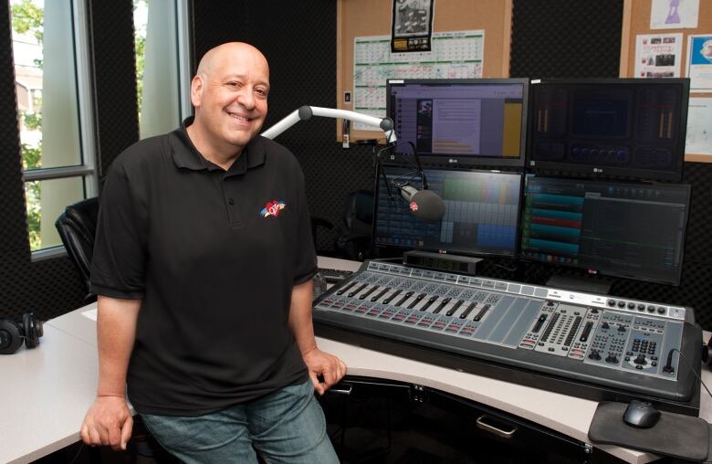 Man in black shirt leaning against equipment, smiling.