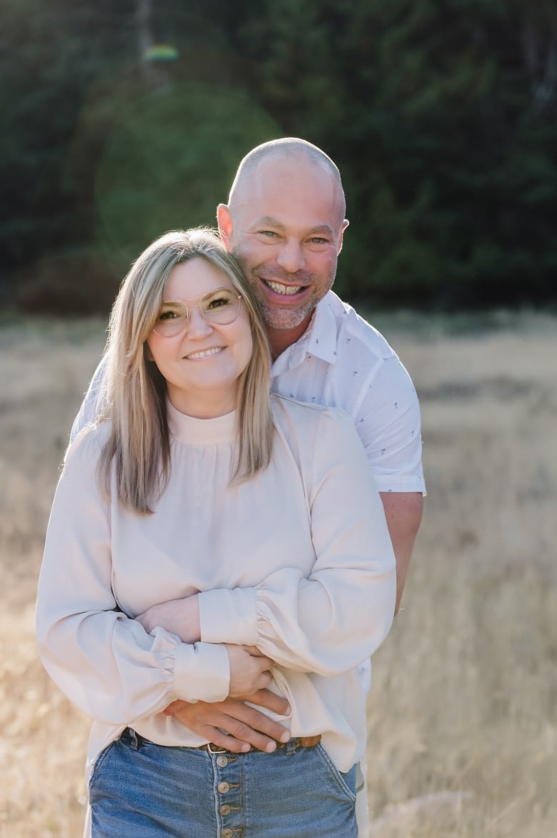 A couple in white shirts hug each other in a field.  