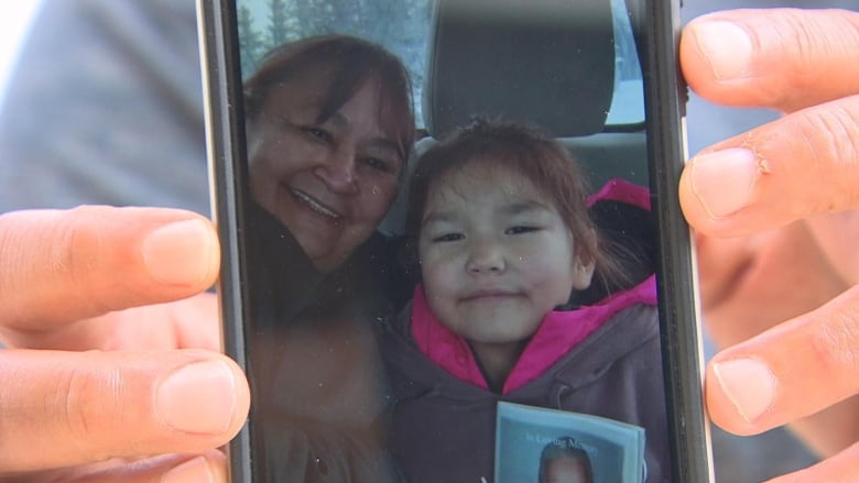 A person's hands hold up a phone, which shows an image of a grandmother and granddaughter.