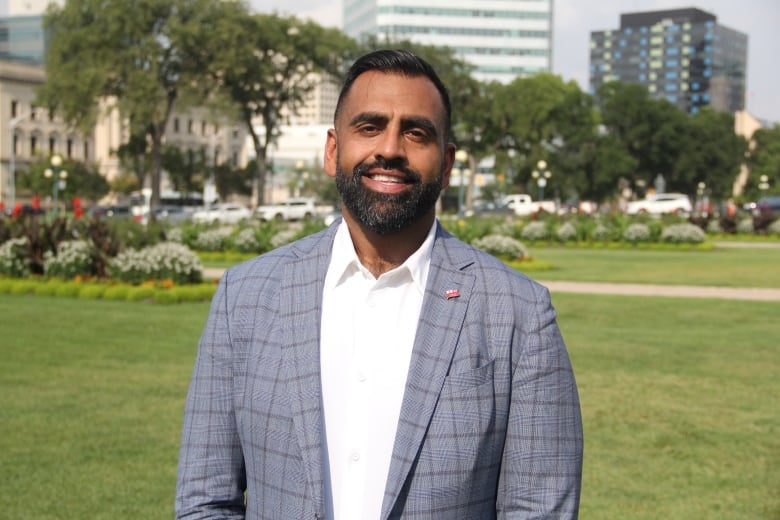 A man in a checkered suit and a white shirt stands on a lawn.