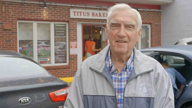 A smiling man with white hair, standing in front of Titus Bakery.