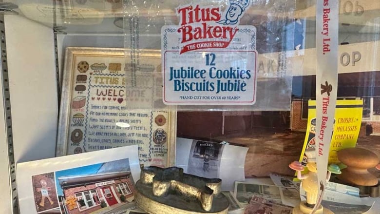 A gingerbread cutter, old cookie bag, cross-stitch welcome greeting and photograph, among other bakery memorabilia in a glass display case.