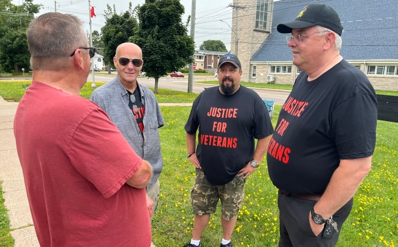 Four men with shirts that say Justice for Veterans standing around talking.