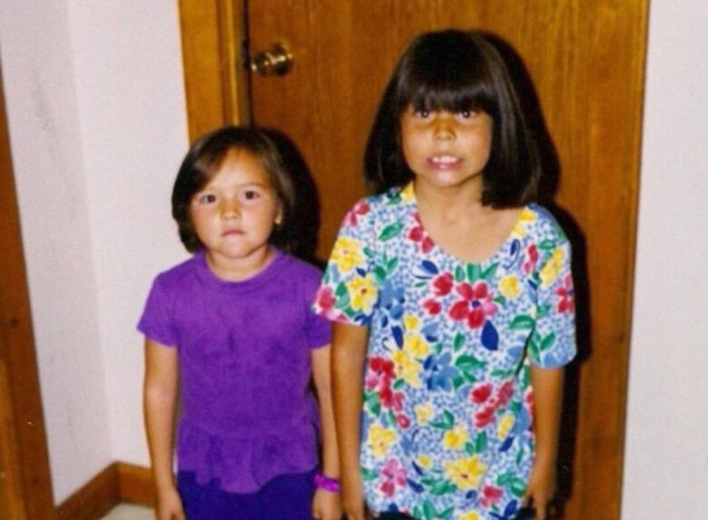 Two little girls stand in front of a wooden door. 