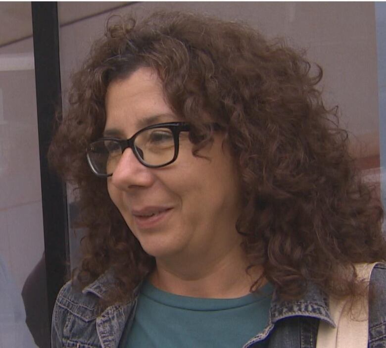 A woman with curly brown hair and glasses is pictured looking away from the camera.