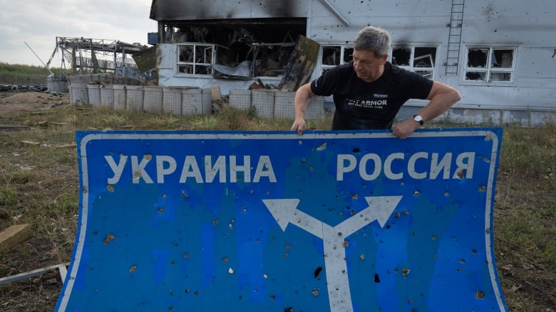 Ukrainian historian Yuri Savchuk holds up a road sign in Sudzha, Russia, last Friday. 