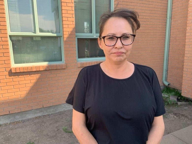 A woman in a black shirt stands in front of a brick wall.