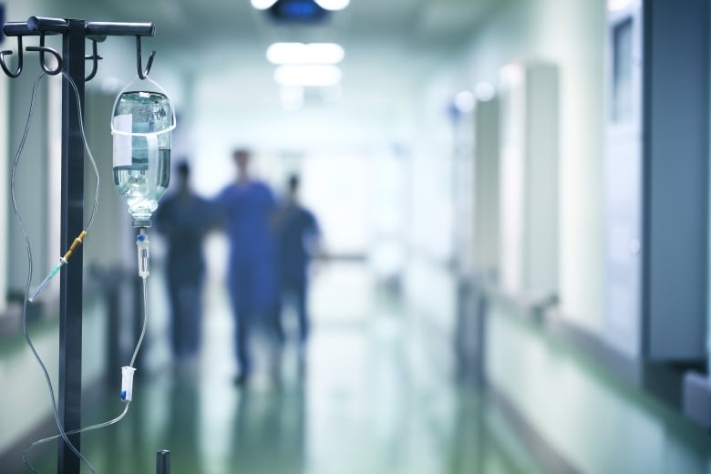 An IV unit is shown in the foreground of a hospital corridor. 