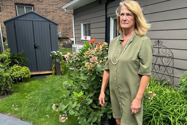 Woman standing surrounded by greenery, a shed and flowers in the background.