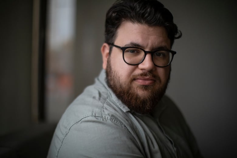 A man with a beard and glasses looks at the camera.